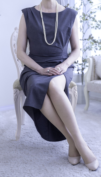 グレーのノースリーブワンピースにパールを合わせた、コンサバティブで気品のある女性会員。