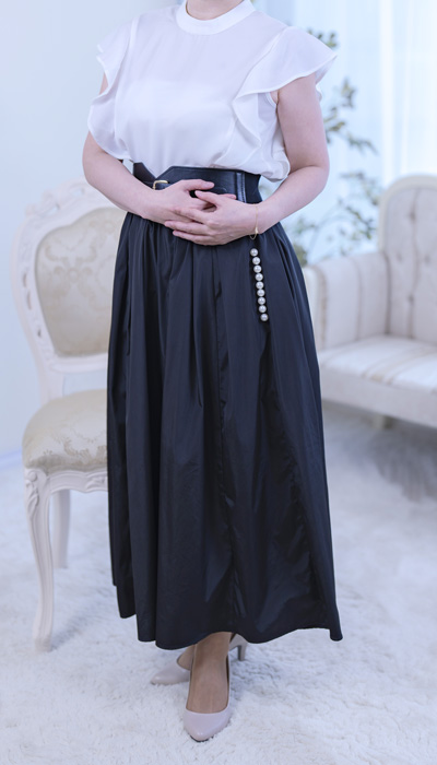 白のブラウスに黒のプリーツロングスカートを合わせた、清楚な中にも芯の強さを感じさせる女性。